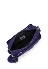 Fioletowa torba crossbody marki Kipling otwarta, ukazująca czarne wnętrze z wieloma przegródkami i markową metką w środku.
