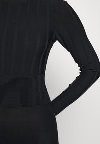 Vêtement noir à manches longues côtelé, présentant des rayures verticales et des sections texturées à la taille et aux manches, offrant une silhouette ajustée.