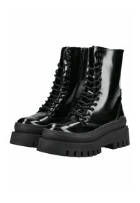 Botas de combate de charol negro con cierre de cordones en la parte delantera, suela gruesa negra y detalle de cremallera. Presenta un grip texturizado para mayor tracción.