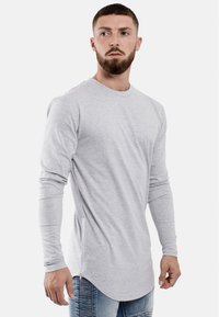 Langärmliges, hellgraues T-Shirt aus weichem Baumwollstoff mit abgerundetem Saum und seitlichem Reißverschluss, tailliert geschnitten.