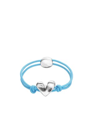 Coletero elástico azul claro con colgante metálico plateado en forma de corazón y cierre ovalado, presentado sobre fondo blanco.