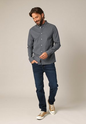 Chemise boutonnée navy avec un petit motif à carreaux blancs, associée à un jean bleu foncé et des baskets beiges. Coupe décontractée et en matériau coton.