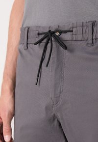 Grå shorts med enkel textur, resår i midjan med svart dragsko och en silverfärgad detaljknapp nära midjan.