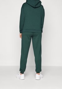 Dark green hoodie and matching joggers made of soft material, featuring a relaxed fit and ribbed cuffs, paired with white sneakers.
