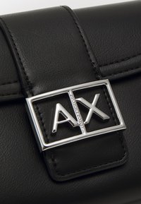 Zwarte leren handtas met een zilveren rechthoekige gesp met het "AX"-logo. Gladde textuur met zichtbare stikseldetails.