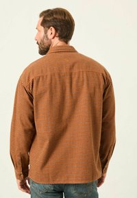 Langärmliges Hemd im orange-braunen Karomuster, mit Knopfmanschette, Kragen und einem einfachen Rückendesign mit dezentem Branding.