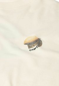 Béžová látka s malým potlačeným vzorom húb a troch listov, pod hubou je rukou písaný text.