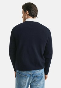 Marineblauer Pullover mit einem schlichten Design, Rundhalskragen und langen Ärmeln, getragen über hellblauen Jeans und zeigt eine weiche Textur.