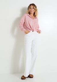 Camisa de rayas rojas y blancas de manga larga atada en la cintura, combinada con jeans blancos de tiro alto y de campana, y sandalias de plataforma marrones.