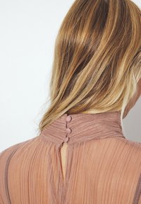 Vilkņu kleita no mīksta rozā auduma, kas aprīkota ar augstu apkakli ar trim pogām aizmugurē un mazu atslēgas caurumu dekoru.