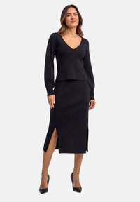 Completo in maglia nera composto da top a maniche lunghe con scollatura a V e gonna al ginocchio con spacchi laterali. Il tessuto testurizzato aggiunge profondità.