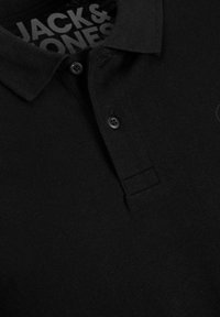 Polo noir avec une texture douce, doté d'un col classique, de deux boutons noirs et du logo "JACK & JONES" affiché à l'intérieur du col.
