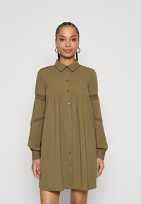 Olive green shirt dress with a button-down front, collared neck, and flared sleeves, featuring textured detailing and lace accents on sleeves.