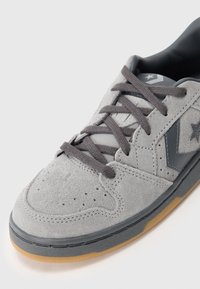Baskets en suède gris avec des accents gris foncé, bout rond, surface texturée et semelle en caoutchouc beige. Comprend des lacets gris et un logo en forme d'étoile.