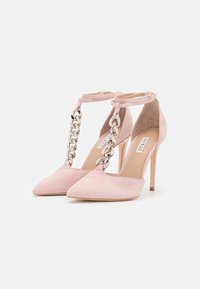 Růžové semišové lodičky s špičatou špičkou a designem T-strap, se stříbrným řetízkovým zdobením. Dokončeny vysokým jehlovým podpatkem.