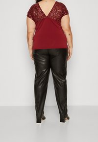 Top burdeos con mangas adornadas con lentejuelas y un escote en V en la espalda, combinado con pantalones de piel sintética negra y zapatos de tacón cuadrado.