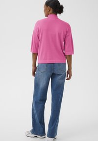 Fuchsienfarbener Rollkragenpullover mit kurzen Ärmeln, kombiniert mit locker sitzenden blauen Jeans und weißen Turnschuhen; glatte Textur und entspannter Schnitt.