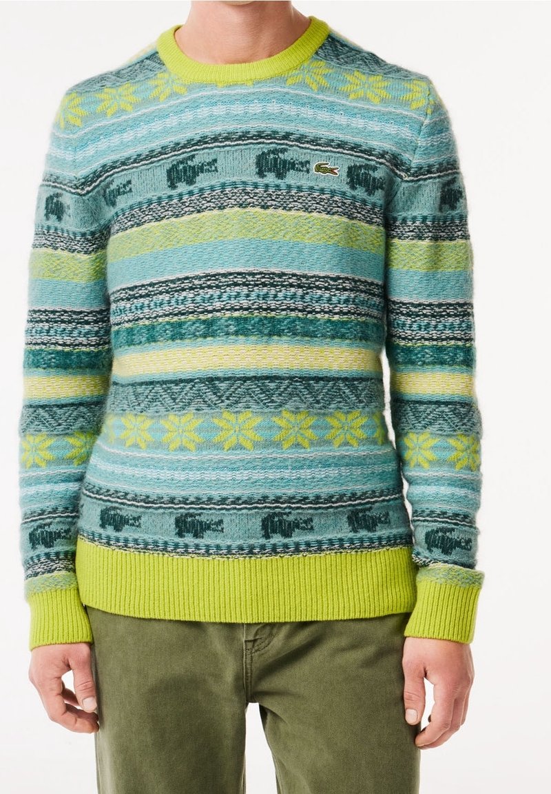 Pletený svetr s vícebarevnými horizontálními pruhy v tyrkysové, zelené a černé. Hlavní lemování a manžety jsou v jasně žluté barvě. Logo Lacoste na hrudi.