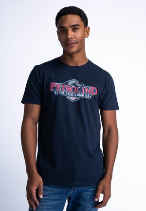 Navy blue cotton t-shirt featuring a red and white graphic print with "PETROL IND" and "KAHUA TRAIL HAWAII U.S.A." in a retro style.