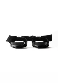 Paire de sandales noires à petits talons avec lanières de cheville nouées en nœuds, photographiées de face sur fond blanc.