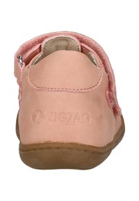 Helle rosa Kinderschuhe mit einer glatten Lederoberfläche, einem Klettverschluss und einem strukturierten Rücken. Mit einem auf der Ferse eingeprägten Logo.