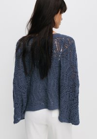 Pull en crochet bleu foncé avec des motifs en openwork géométriques élaborés, des manches longues amples et une coupe décontractée.