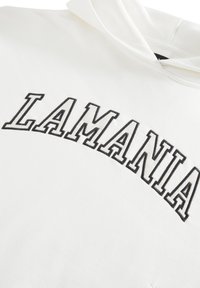 Biela mikina s kapucňou s vyšívaným nápisom "LAMANIA" v čiernych veľkých písmenách naprieč hrudníkom. Obsahuje kapucňu so šnúrkou a jemnú textúru látky.