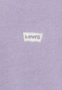 Suéter de punto lila con un tejido texturizado y un parche del logo de Levi's en blanco con letras moradas, situado en el centro.