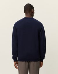 Sötétkék pulóver puha anyagból, kerek nyakkivágással, hosszú ujjakkal, bordás mandzsettákkal és aljjal, hátulról bemutatva.