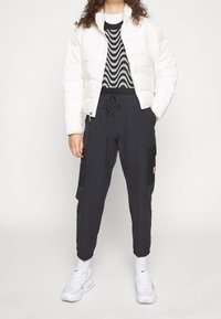 Chaqueta de plumas blanca, suéter negro con patrón de zigzag, pantalones cargo negros con bolsillos, zapatillas blancas con acentos negros y calcetines blancos.