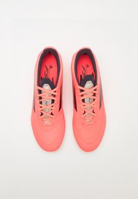 Bright coral athletic shoes with a textured upper, thin black stripes, and standard lacing. Features a cushioned tongue and padded collar.
