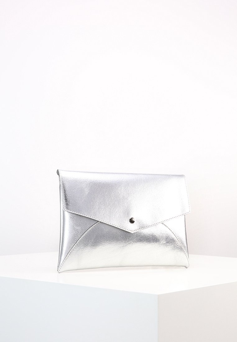 Pochette argentée métallique de style enveloppe avec fermeture à bouton-pression sur le devant, posée sur une surface blanche sur un fond uni.