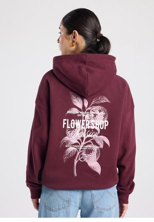 Bordeauxrode hoodie met grote witte bloemengrafiek en tekst op de achterkant. Heeft een losse pasvorm met een capuchon met trekkoord en geribbelde mouwen.