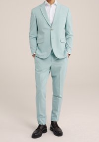 Light blue suit made of smooth fabric, featuring a single-button closure, two front pockets, and matching tailored trousers. Black dress shoes.