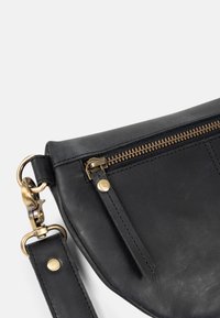 Black leather bag with gold zipper and clasp, featuring a leather strap attached to a metal ring on a white background.