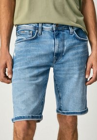 Pantalones cortos de mezclilla azules claros con un acabado desgastado, puños enrollados y bolsillos. Presenta un cierre de botón de metal y cremallera para mayor funcionalidad.