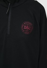 Svart zip-up hoodtröja med en strukturerad yta, med en rund röd lapplogotyp märkt "DBU" på bröstet.