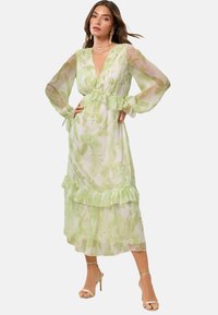 Rochie maxi cu imprimeu floral verde deschis, cu m�âneci lungi din material transparent, talie volanată și detalii la tiv. Fabricată dintr-un material ușor și fluid.