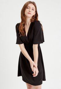 Abito nero a maniche corte con scollatura a V e vita elastica. Realizzato in tessuto morbido e leggero, presenta una silhouette rilassata e lunghezza sopra il ginocchio.