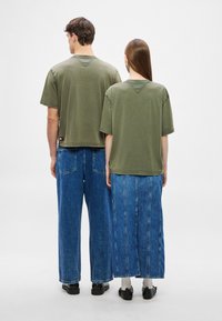 Tricouri verzi măslinii din bumbac cu mâneci scurte, asortate cu pantaloni din denim și o fustă lungă. Cusături vizibile și o etichetă mică la tiv.