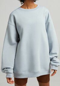 Lichtblauwe oversized sweatshirt met een geribde ronde halslijn, verlaagde schouders en lange mouwen. Zachte textuur, minimalistisch ontwerp.