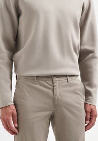 Beige langemouwshirt met een gestructureerde afwerking, gecombineerd met lichtbeige broek met knoopsluiting en een gladde stof.