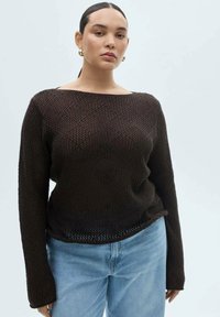 Brun stickad tröja med bred halsringning och långa ärmar, med en strukturerad, öppen vävdesign och en avkopplad passform. Stylingen kompletteras med ljusblå jeans.