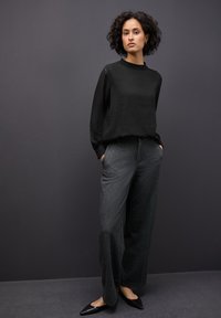 Blusa negra texturizada con mangas abullonadas, combinada con pantalones de pierna ancha de cintura alta en gris oscuro y zapatos planos negros de punta.