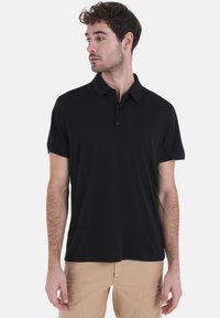 Zwarte polo met een kraag, korte mouwen en een knoopsluiting; heeft een gladde stof en een slim-fit silhouet.