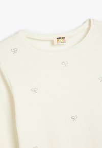 Witte geribbelde lange mouwen shirt voor kinderen, met kleine hartpatronen gemaakt van zilveren studs, een ronde hals en een zachte stofstructuur.