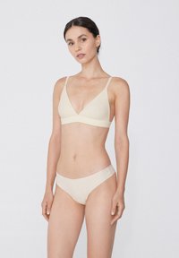Béžový bezdrátový bralet s trojúhelníkovým tvarem, tenkými nastavitelnými ramínky a odpovídajícími bikinovými kalhotkami. Hladká tkanina s jemnou strukturou.