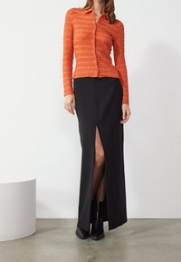 Camicia a maniche lunghe arancione a trama con colletto abbottonato abbinata a una gonna maxi nera con spacco frontale e stivali neri alla caviglia.