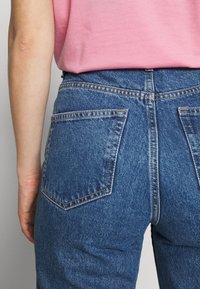 Modré džíny s vysokým pasem, které mají dvě zadní kapsy, precizní šev a mírně vybledlý texture.