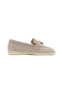 Mocassin en daim beige avec semelle basse crème et un élément décoratif en métal sur le dessus, présenté en vue latérale sur fond blanc.